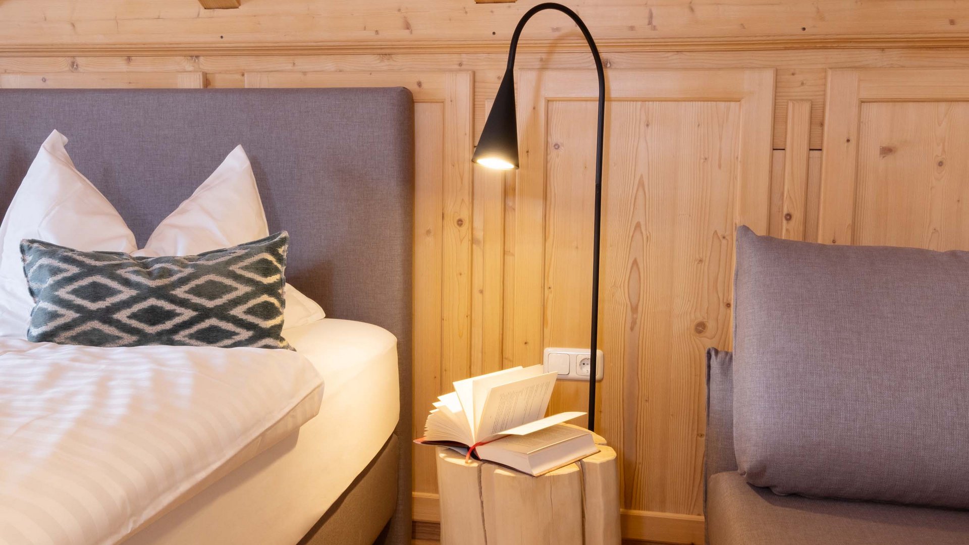 Hotel and holiday apartment in Allgäu, Oberstdorf Cozy bedroom with bed, pillows, log bedside table and reading lamp