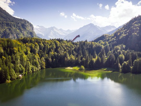 Plant euren Urlaub in Oberstdorf Bergsee mit grünem Wald und Sprungschanze in den Alpen bei klarem Himmel