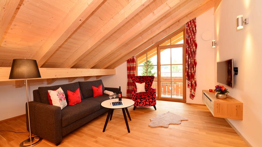 Hotel and holiday apartment in Allgäu, Oberstdorf Cozy living room with wooden beams, sofa, armchair and balcony view