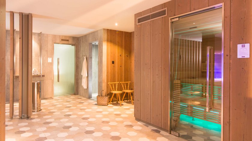 Hotel and holiday apartment in Allgäu, Oberstdorf Modern sauna area with wooden paneling, glass door, and two wooden chairs
