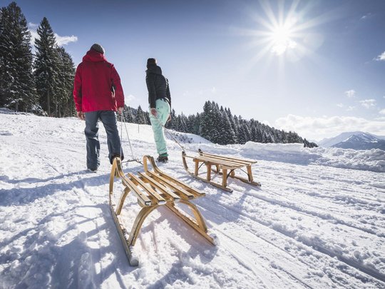 Hahnenköpfle: Ferienwohnung, Lodge und Hotel in Oberstdorf Zwei Personen ziehen Schlitten durch verschneite Berglandschaft bei Sonnenschein