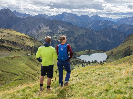 Plant euren Urlaub in Oberstdorf Zwei Wanderer blicken auf einen Bergsee und Gebirgspanorama mit Wolken