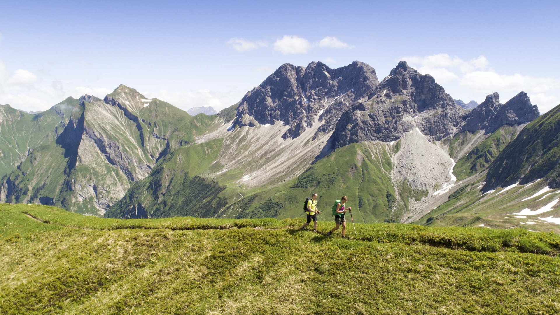 Plant euren Urlaub in Oberstdorf Zwei Wanderer auf grüner Bergwiese mit Alpen und blauem Himmel im Hintergrund