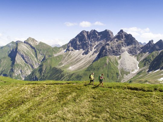 Hahnenköpfle: Ferienwohnung, Lodge und Hotel in Oberstdorf Zwei Wanderer auf grüner Bergwiese mit Alpen und blauem Himmel im Hintergrund