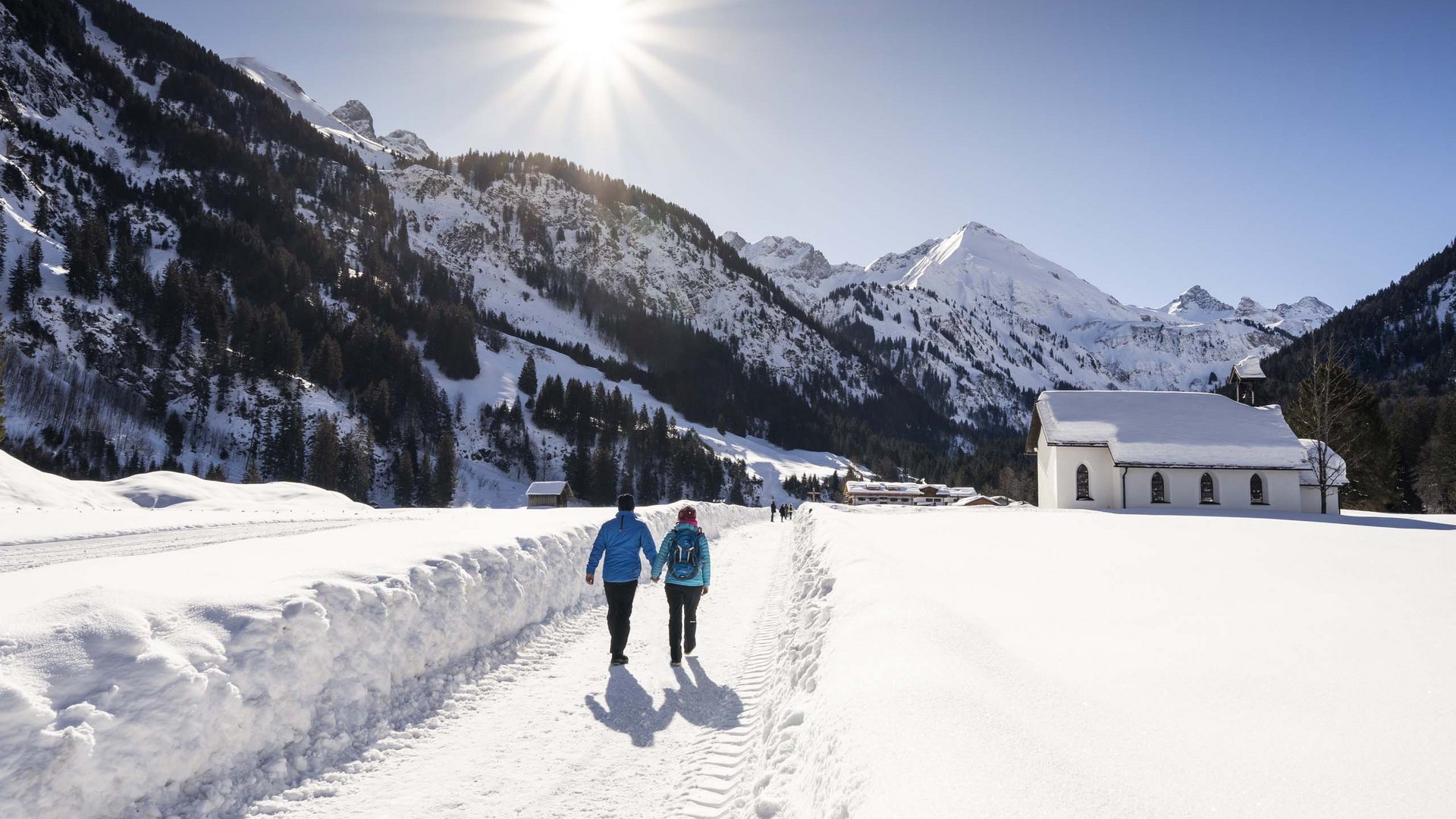 Plant euren Urlaub in Oberstdorf Paar wandert auf verschneitem Weg in Berglandschaft bei Sonnenschein