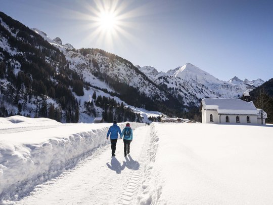 Hahnenköpfle: Ferienwohnung, Lodge und Hotel in Oberstdorf Paar wandert auf verschneitem Weg in Berglandschaft bei Sonnenschein
