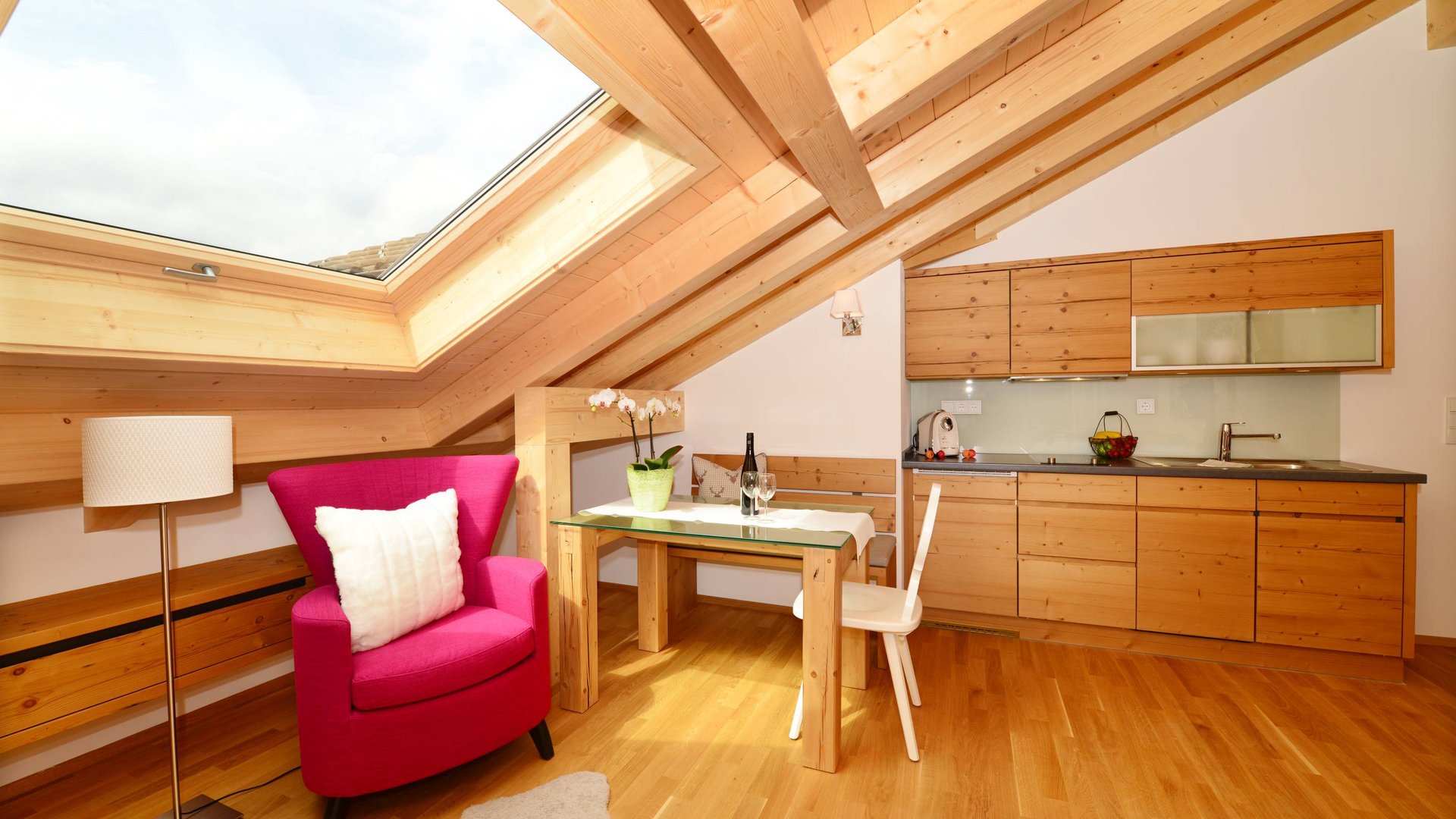 Hotel and holiday apartment in Allgäu, Oberstdorf Cozy attic kitchen with wooden furniture and pink armchair under skylight window