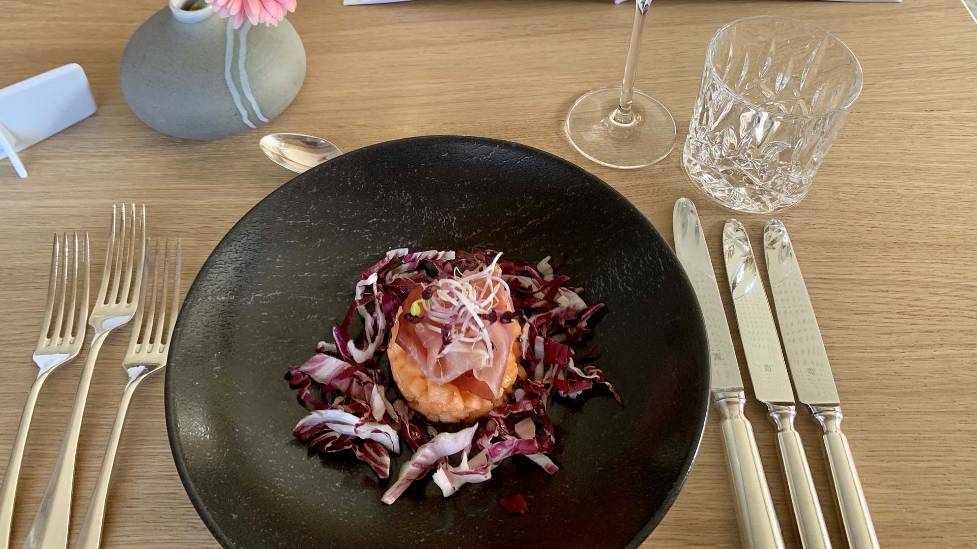 Euer Hotel in Oberstdorf mit Halbpension Vorspeise mit rohem Fisch auf schwarzem Teller, Blumendeko und Getränken auf Tisch