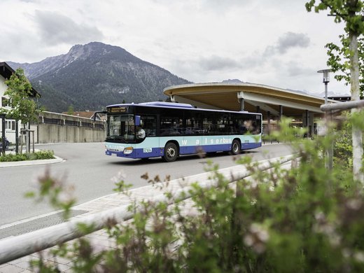 Plant euren Urlaub in Oberstdorf Blauer Walserbus an einer Haltestelle vor Bergen unter bewölktem Himmel