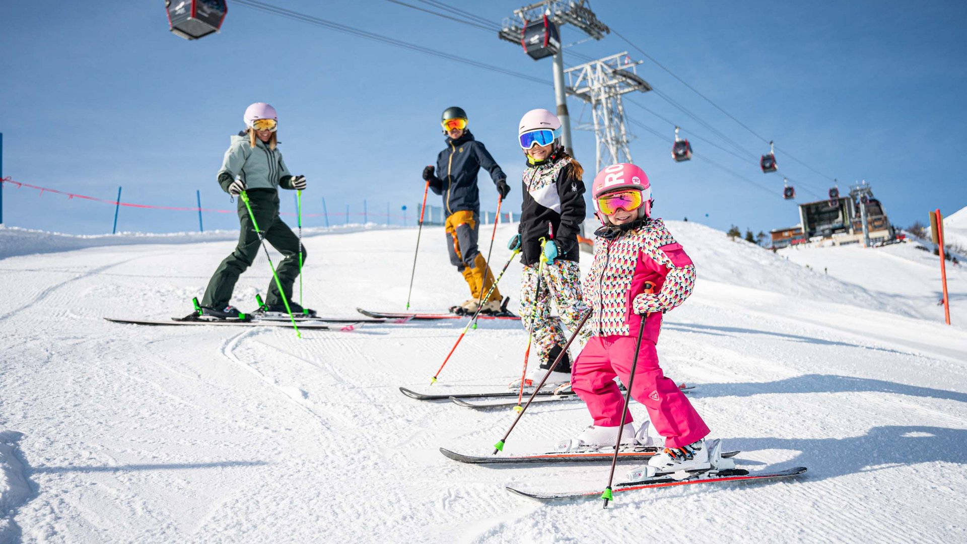 Plant euren Urlaub in Oberstdorf Familie mit Kindern beim Skifahren auf sonniger Piste mit Seilbahn im Hintergrund