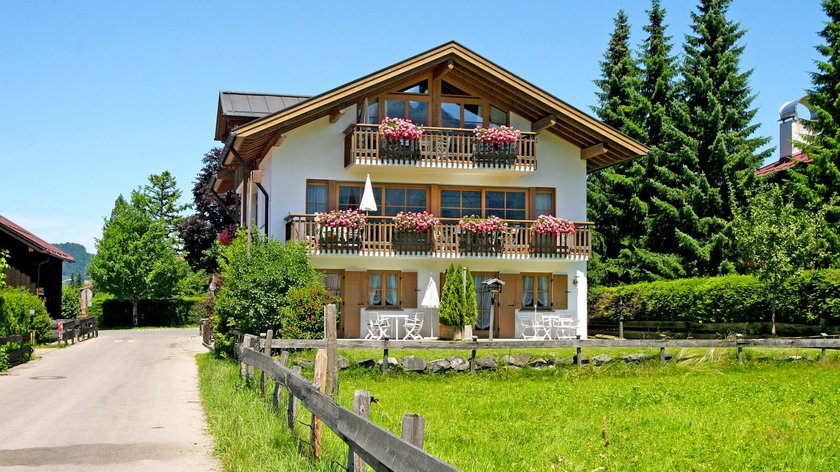 Hotel and holiday apartment in Allgäu, Oberstdorf House with balconies and flowers by a country road surrounded by greenery