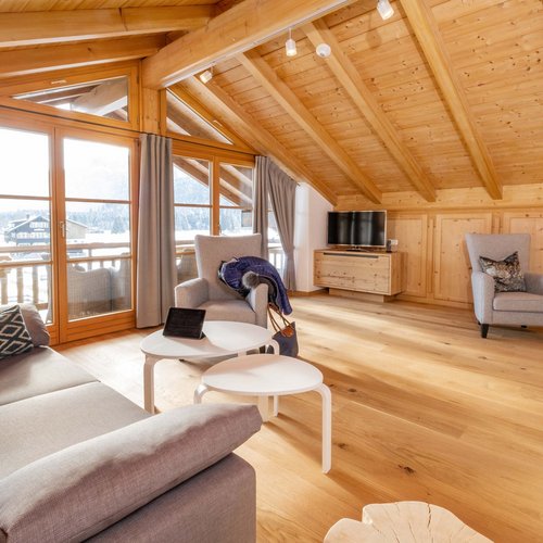 Hahnenköpfle: Ferienwohnung, Lodge und Hotel in Oberstdorf Gemütliches Wohnzimmer mit Holzdecke, Sofas, Sesseln und großem Fenster zum Balkon