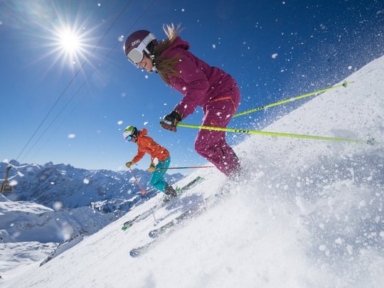Hahnenköpfle: Ferienwohnung, Lodge und Hotel in Oberstdorf Zwei Skifahrer in bunter Kleidung fahren auf schneebedecktem Berg im Sonnenschein